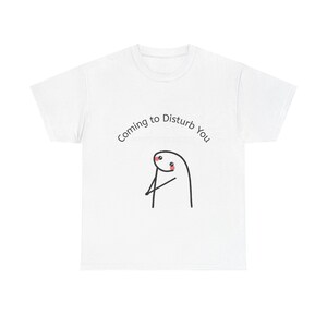 May include: A white short-sleeved t-shirt featuring a black line-art illustration of a simple stick figure character with pink cheeks. Above the character, the text reads Coming to Disturb You in a clean, black, sans-serif font.