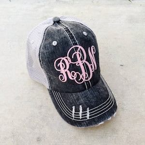 May include: A black and white distressed trucker hat with a pink monogram "RBM" embroidered on the front.