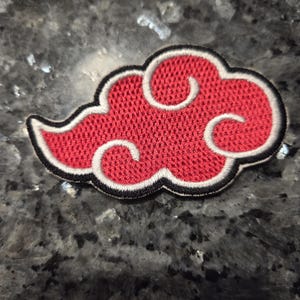 May include: An embroidered patch in the shape of a stylized cloud. The cloud features a vibrant red textured center with white and black stitched borders, creating a distinct layered outline effect for the iconic anime-inspired design.