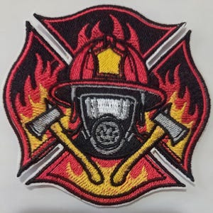May include: An embroidered patch featuring a red and yellow Maltese cross shape with flames. In the center, a red firefighter helmet sits above a black and white gas mask, flanked by two crossed silver axes with yellow handles on a black background.