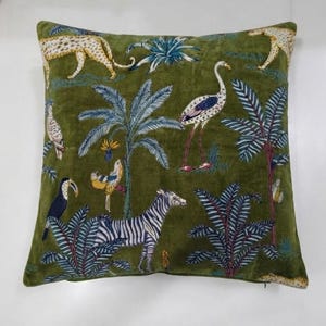 May include: A square throw pillow featuring a deep olive green velvet fabric with a printed pattern of various animals and tropical plants. The design includes a zebra, a leopard, a crane, a toucan, and palm trees in shades of blue and yellow.