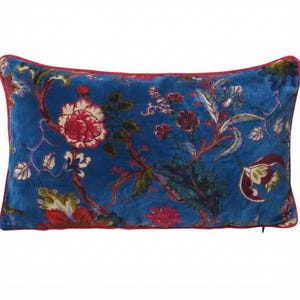 Peut inclure: Un coussin rectangulaire en velours présentant un fond bleu vif avec un motif floral multicolore dans des tons de rouge, rose, vert et blanc. Le coussin est bordé d'un passepoil rouge uni et fin sur les quatre côtés.