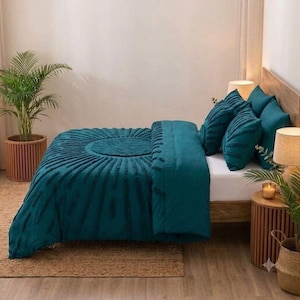 May include: A teal bedding set featuring a textured sunburst pattern on the duvet cover and matching throw pillows. The set is displayed on a bed with a wooden headboard, flanked by two wooden side tables with lamps and potted green plants.