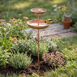 May include: A copper-coloured metal bird feeder and bath combination featuring two stacked circular bowls on a thin stand. The top bowl holds birdseed, while the lower bowl contains water. A small metal bird figure is attached to the central stem.