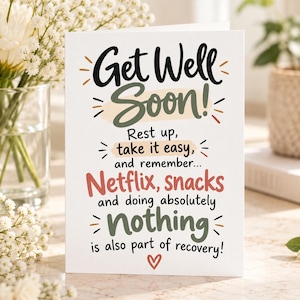 Può includere: Un biglietto d'auguri bianco con testo nero, verde oliva e corallo che recita: Get Well Soon! Rest up, take it easy, and remember... Netflix, snacks and doing absolutely nothing is also part of recovery! Un piccolo cuore rosso è in basso.