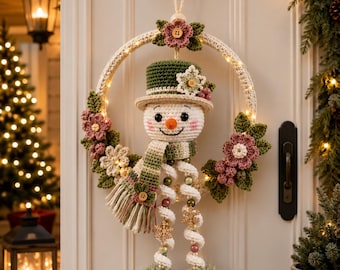 May include: A crocheted snowman wreath featuring a green top hat, a striped scarf, and dangling legs with pom-poms. The circular frame is adorned with crocheted pink flowers, green leaves, and small wooden buttons, illuminated by integrated warm white fairy lights.