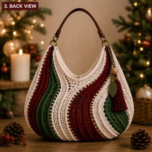 Può includere: Una borsa a mano all'uncinetto in stile hobo con un motivo ondulato in filato color crema, rosso scuro e verde bosco. La borsa presenta un unico manico in pelle marrone fissato con anelli metallici e un ciondolo decorativo con una perla in legno, una foglia e una nappa rossa.