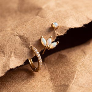 May include: A set of three gold earrings including a small hoop earring with embedded clear stones, a stud earring with three marquise-cut opal stones arranged in a fan shape, and a single small round opal stud earring.