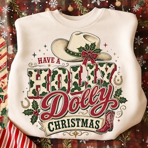 May include: A cream-colored crewneck sweatshirt featuring a graphic print of a cowboy hat adorned with holly, the text "HAVE A HOLLY DOLLY CHRISTMAS," two gold horseshoes, and a red cowboy boot, all surrounded by decorative holly and star accents.