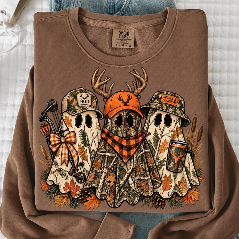 May include: A brown crewneck sweatshirt featuring a graphic of three ghosts wearing camouflage hats. The ghosts are decorated with autumn leaves, a bow, a compound bow, a plaid scarf, and a mug. The text reads BOO and SPOOKY SEASON.