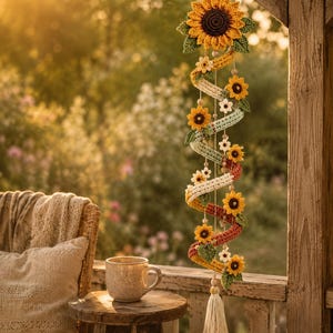 Könnte beinhalten: Eine hängende Spiraldekoration aus gehäkeltem Garn, mit einer großen Sonnenblume an der Spitze, kleineren Sonnenblumen, weißen Blüten und grünen Blättern entlang der Länge, abgeschlossen mit einer cremefarbenen Quaste am unteren Ende.