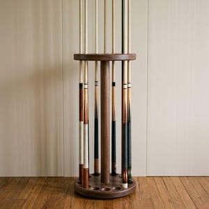 Peut inclure: Un support de sol circulaire en bois conçu pour contenir plusieurs queues de billard. Le support comprend un pilier central, un anneau supérieur avec des fentes pour les flèches et une base avec des encoches circulaires pour les talons.