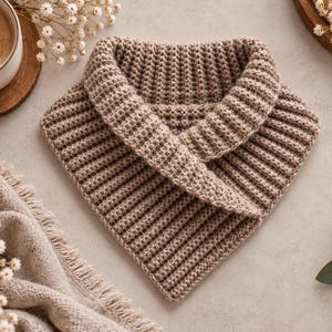 Puede incluir: Un calentador de cuello de color marrón claro con forma triangular y un patrón de ganchillo acanalado y texturizado. El accesorio presenta un diseño de cuello doblado y está hecho de hilo suave, con un punto uniforme en toda la pieza.