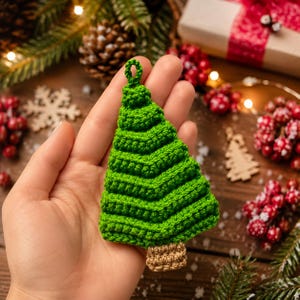 May include: A small, triangular Christmas tree ornament made of green crocheted yarn with a textured, layered design. The tree features a small loop at the top for hanging and a rectangular brown crocheted base representing the tree trunk.