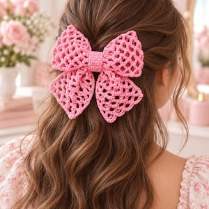May include: A large, bright pink hair bow crafted with an open, lattice-style crochet pattern. The bow features a solid, tightly stitched centre band and is secured to the hair, showcasing a textured, geometric design with four distinct loops.