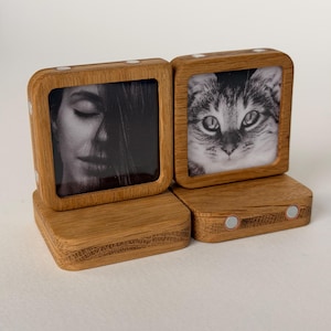 Op de afbeelding: Twee vierkante houten frames met lichtbruine nerf, elk gemonteerd op een bijpassende houten voet. Het linker frame toont een zwart-wit portret van een persoon met gesloten ogen, terwijl het rechter frame een zwart-wit close-up van een kat toont.