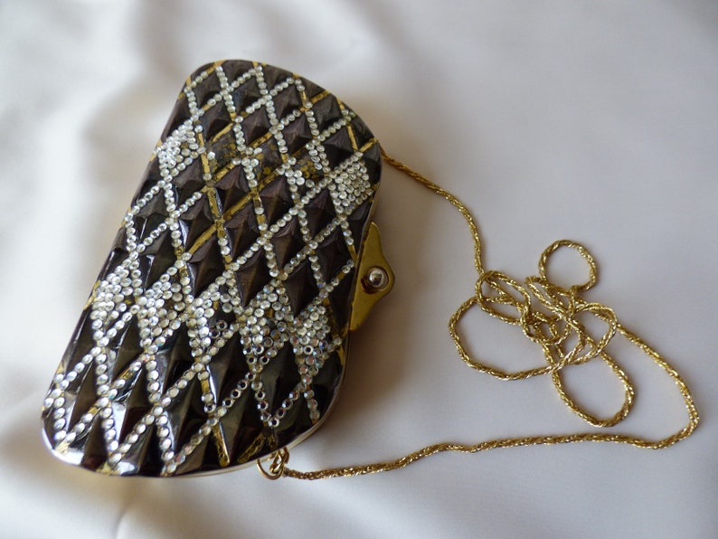 Peut inclure: Un sac de soir&eacute;e noir et or avec un motif en diamant et une bandouli&egrave;re en cha&icirc;ne dor&eacute;e.