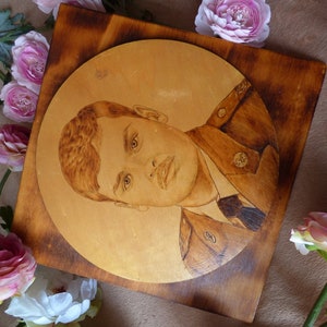 Peut inclure: Une plaque en bois avec un portrait circulaire grav&eacute; d'une personne en uniforme militaire. La plaque est entour&eacute;e de fleurs roses.