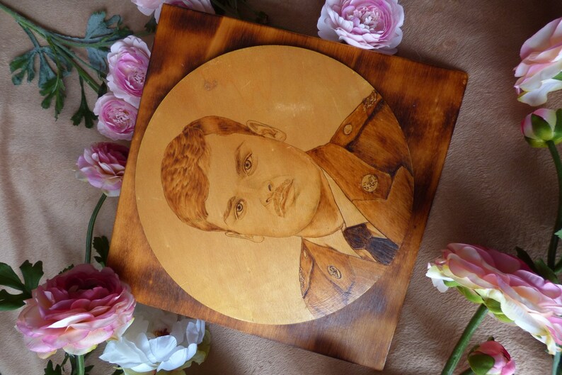 Peut inclure: Une plaque en bois avec un portrait circulaire grav&eacute; d'une personne en uniforme militaire. La plaque est entour&eacute;e de fleurs roses.