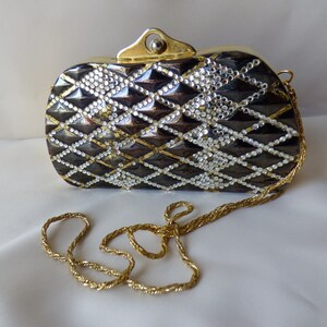 Peut inclure: Un sac de soir&eacute;e noir et argent avec une bandouli&egrave;re en cha&icirc;ne dor&eacute;e. Le sac est recouvert de strass et pr&eacute;sente un motif matelass&eacute;.