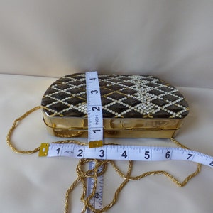Peut inclure: Une bourse &agrave; cha&icirc;ne dor&eacute;e avec un motif g&eacute;om&eacute;trique noir et blanc et des accents de perles blanches. La bourse mesure 10 cm de large et 5 cm de haut.