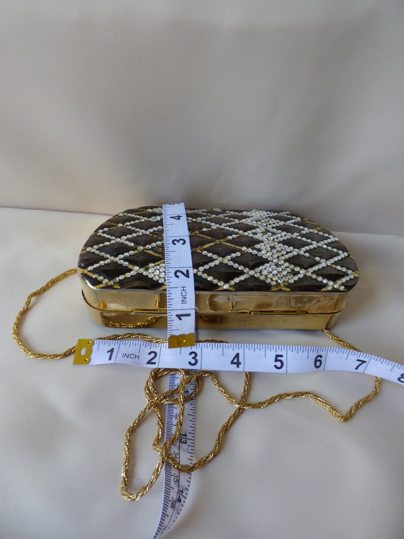 Peut inclure: Une bourse &agrave; cha&icirc;ne dor&eacute;e avec un motif g&eacute;om&eacute;trique noir et blanc et des accents de perles blanches. La bourse mesure 10 cm de large et 5 cm de haut.