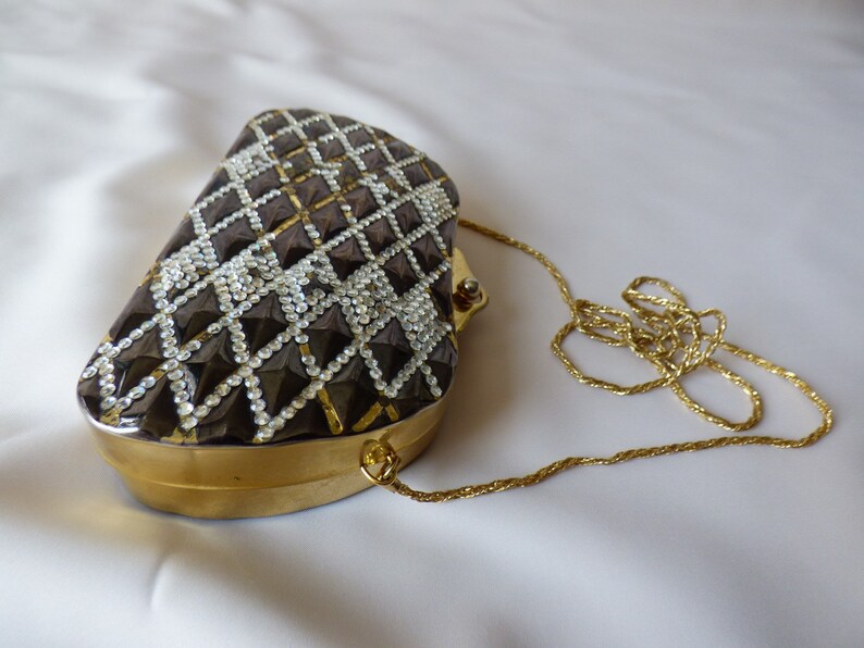 Peut inclure: Un sac de soir&eacute;e noir et or avec un motif en forme de diamant et une bandouli&egrave;re en cha&icirc;ne dor&eacute;e.