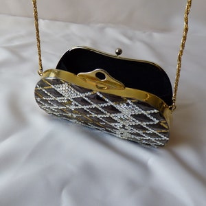 Peut inclure: Un sac &agrave; main de soir&eacute;e avec une bandouli&egrave;re en cha&icirc;ne dor&eacute;e, un int&eacute;rieur en velours noir et un ext&eacute;rieur transparent orn&eacute; de bijoux. Le sac est d&eacute;cor&eacute; d'un motif g&eacute;om&eacute;trique de strass blancs.