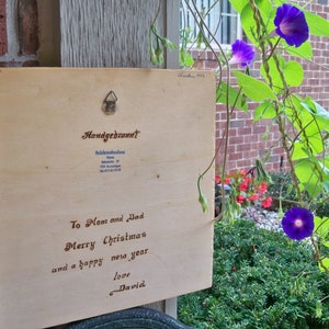 Peut inclure: Une pancarte en bois avec un message manuscrit qui dit "To Mom and Dad Merry Christmas and a happy new year love David". La pancarte est accroch&eacute;e &agrave; un mur de briques avec une vigne de fleurs de gloire du matin violettes qui pousse le long du mur.