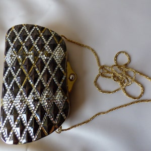 Peut inclure: Un sac de soir&eacute;e noir et or avec un motif en forme de diamant et une bandouli&egrave;re en cha&icirc;ne dor&eacute;e.