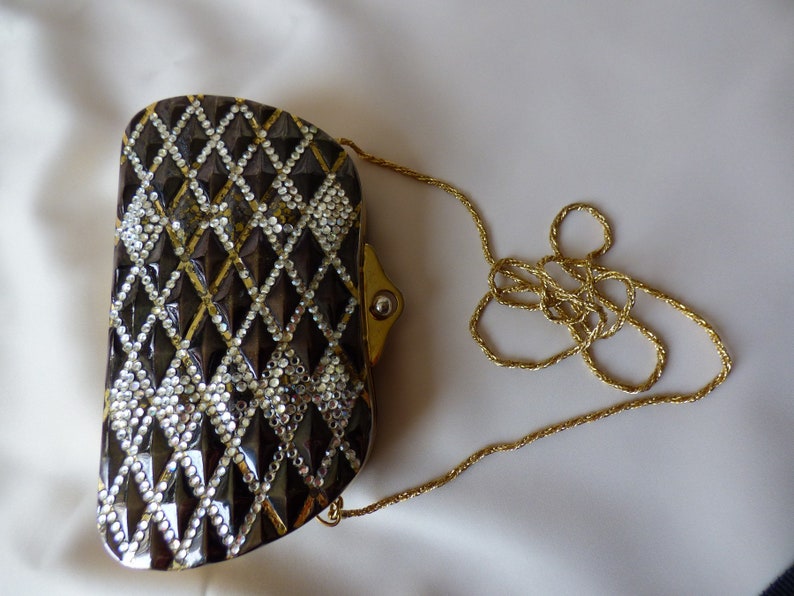 Peut inclure: Un sac de soir&eacute;e noir et or avec un motif en forme de diamant et une bandouli&egrave;re en cha&icirc;ne dor&eacute;e.