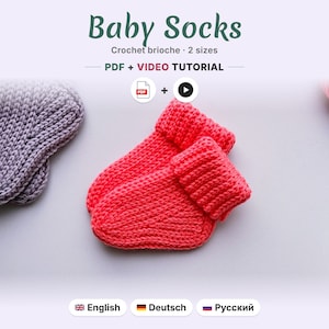 May include: A pair of bright coral crochet baby socks with a folded cuff, accompanied by a partial view of a grey crochet item. The text reads Baby Socks, Crochet brioche, 2 sizes, PDF + VIDEO TUTORIAL, English, Deutsch, and Russian.