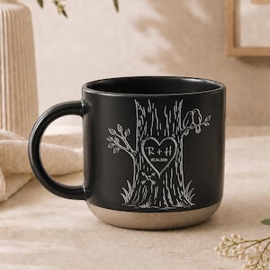 May include: A matte black ceramic mug featuring a white line-art illustration of a tree trunk with a heart carving containing the initials R + H and the date 07.14.2020, with two small birds perched on a branch and two crossed arrows below.