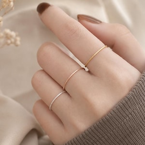 Puede incluir: Tres anillos finos y apilables colocados en tres dedos. El anillo superior es dorado, el del medio es de oro rosa y el anillo inferior es plateado. Cada banda presenta un acabado liso y pulido con un perfil delicado y delgado.