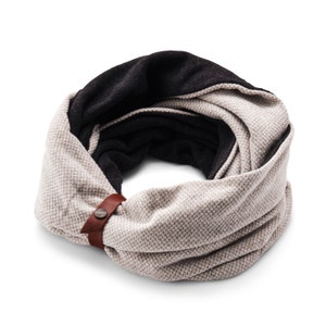 Może przedstawiać: Rewersyjna szalika z brązowym paskiem skórzanym i metalowym guzikiem. Jedna strona jest jasnobeżowa z subtelnym wzorem, a druga strona jest czarna.