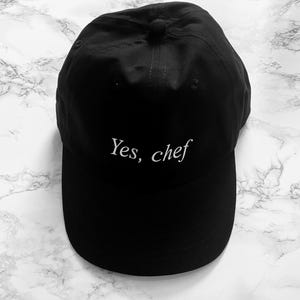 May include: Black baseball cap with white embroidery that reads "Yes, chef".