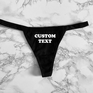 May include: Black lace thong underwear with the text "CUSTOM TEXT" printed in white.