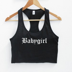 May include: Black racerback tank top with a white "Babygirl" graphic in a gothic font.