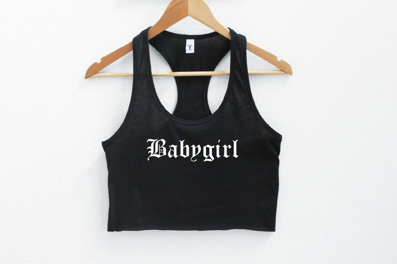 May include: Black racerback tank top with a white "Babygirl" graphic in a gothic font.