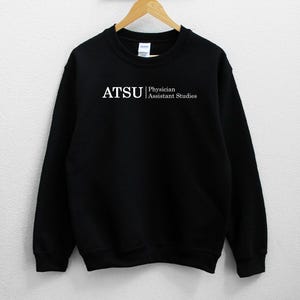 以下が含まれることがあります： 白い文字で「ATSU Physician Assistant Studies」と書かれた黒いスウェットシャツです。