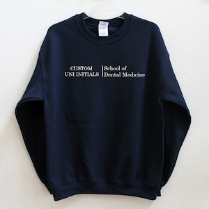 Pode incluir: Camisola de cor azul marinho com texto branco que diz "CUSTOM UNI INITIALS | School of Dental Medicine".
