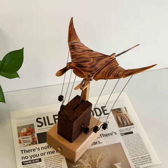 A hand-carved wooden manta ray that actually moves via a hidden mechanical automata mechanism — the kind of desk object that stops every visitor cold.
