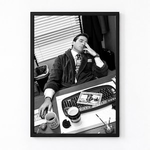 May include: A black and white framed print featuring a person in a bathrobe and tie sitting at a desk with a computer keyboard, a mug labeled World's Best Boss, and a small photograph. The person has one hand on their forehead in a tired pose.