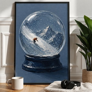 Op de afbeelding: Een ingelijste kunstdruk met een olieverfschilderij van een sneeuwbol met daarin een skiër in een oranje jas die een besneeuwde berghelling afdaalt. De achtergrond van de bol is een diepblauwe lucht met witte stippen als sneeuw.