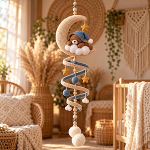 May include: A hanging mobile featuring a crocheted brown bear wearing a blue nightcap, resting on a white cloud and a crescent moon. The structure includes a spiral design with blue and beige yarn, yellow stars, blue spheres, and white pom-poms.