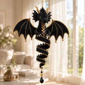 Op de afbeelding: Een zwarte gehaakte draak als ornament met goudkleurige hoorns, vleugelranden en borstschubben. De draak heeft groene ogen, een lange gekrulde staart en hangt aan een ketting met een zwarte traanvormige kraal aan de onderkant van de staart.