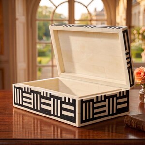May include: A rectangular storage box with an open lid, featuring a cream-colored base with a contrasting black geometric pattern of vertical and horizontal lines. The interior is smooth and cream-colored, matching the exterior frame and lid.