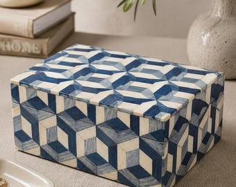 May include: A rectangular storage box featuring a geometric pattern of blue and cream-colored inlaid pieces. The box has a hinged lid and a smooth finish, with the repeating pattern covering the top and all four visible sides of the container.