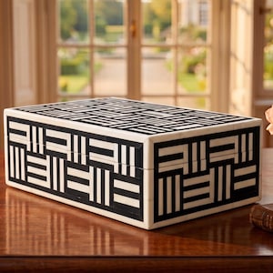 May include: A rectangular storage box featuring a high-contrast black and white geometric pattern. The exterior is decorated with an intricate, repeating arrangement of alternating horizontal and vertical stripes, creating a structured, woven-like visual effect.