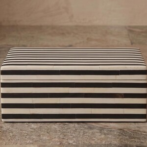 May include: A rectangular storage box featuring a high-contrast pattern of horizontal black and white stripes. The box has a flat lid and a structured, boxy shape with visible seams between the individual rectangular pieces forming the striped exterior.